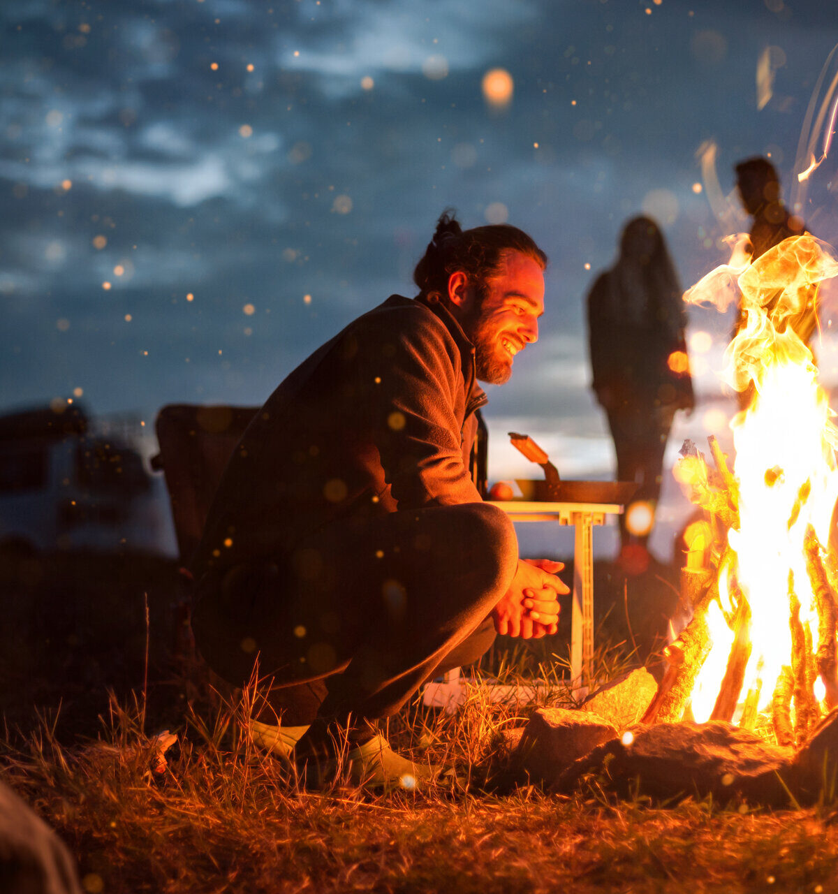 Lächelnder Mann neben einem Lagerfeuer in der Dunkelheit