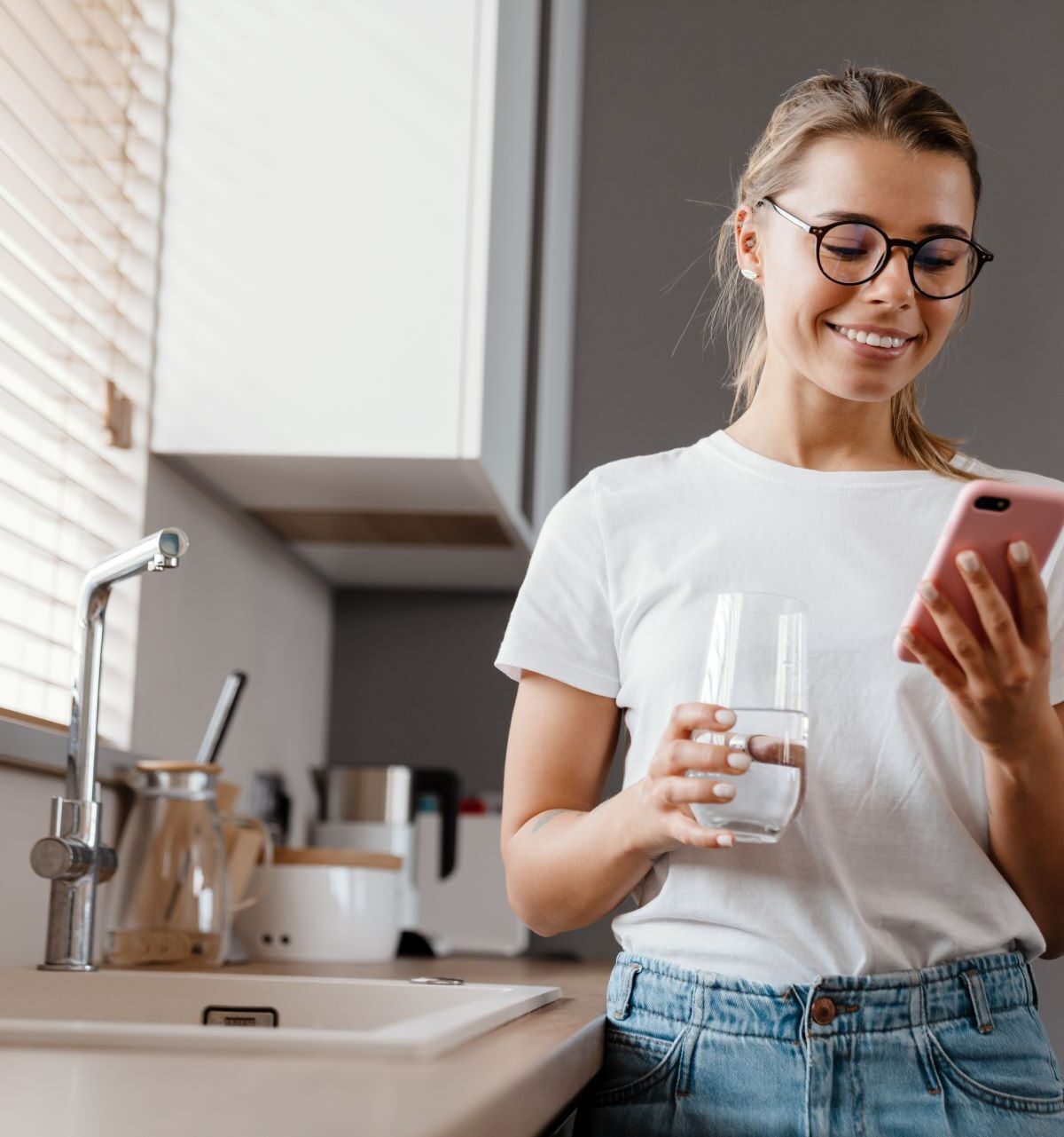 Schönes glückliches Mädchen, das Wasser trinkt, während es ein Mobiltelefon benutzt