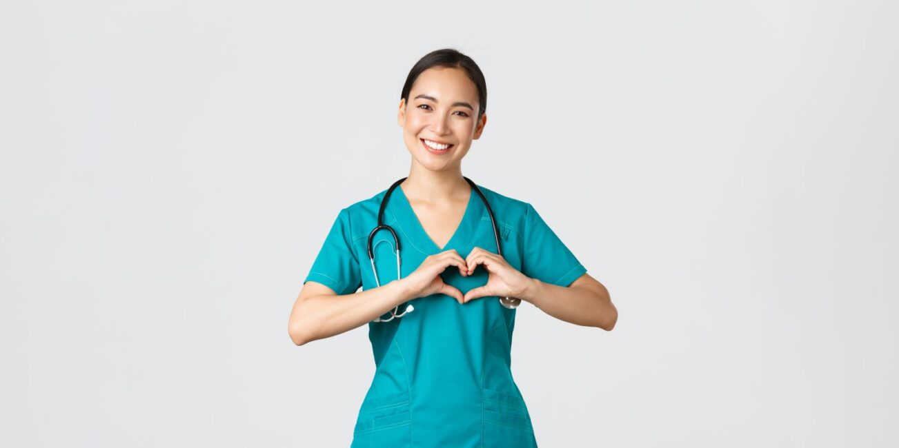 Fürsorgliche asiatische Ärztin, weibliche Krankenschwester in Kittel, Pflegefachkraft, die Herzgeste zeigt und lächelt, die sich mit Liebe um Patienten kümmert