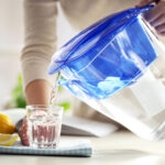 Eine Frau gießt sich Wasser aus einem Wasserfilter