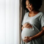 Eine glückliche schwangere Frau in grauem Kleid hält ihre Hände auf ihren Bauch. Was gilt rechtlich für Elternzeit? Ein Anwalt für Arbeitsrecht gibt Antworten.