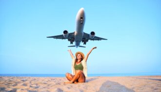 Frau sitzt am Strand mit Blick auf tief fliegendes Flugzeug – Reisen mit Lufthansa Status genießen